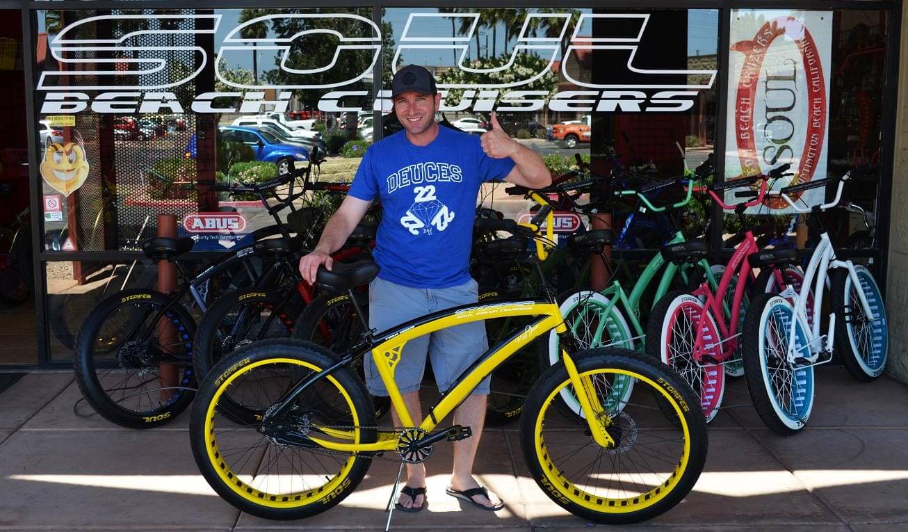 Man posing with yellow bicycle outside store.
