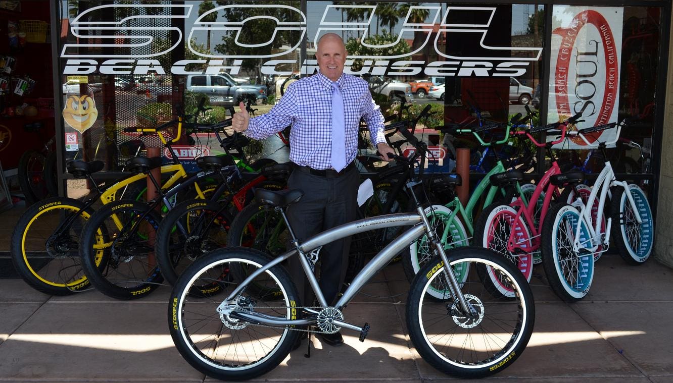 Man posing with bicycles outside bike shop.