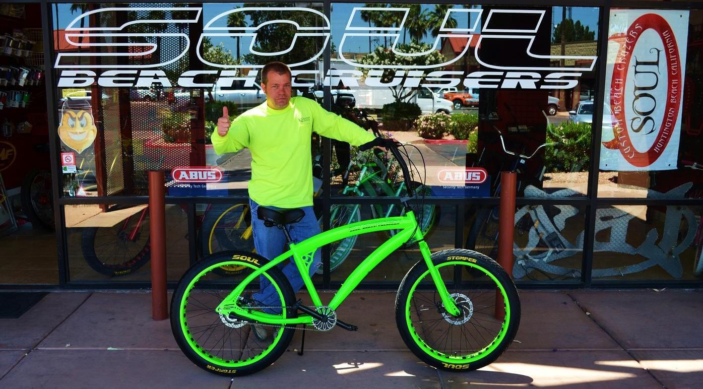 Man with neon green bicycle outside shop.