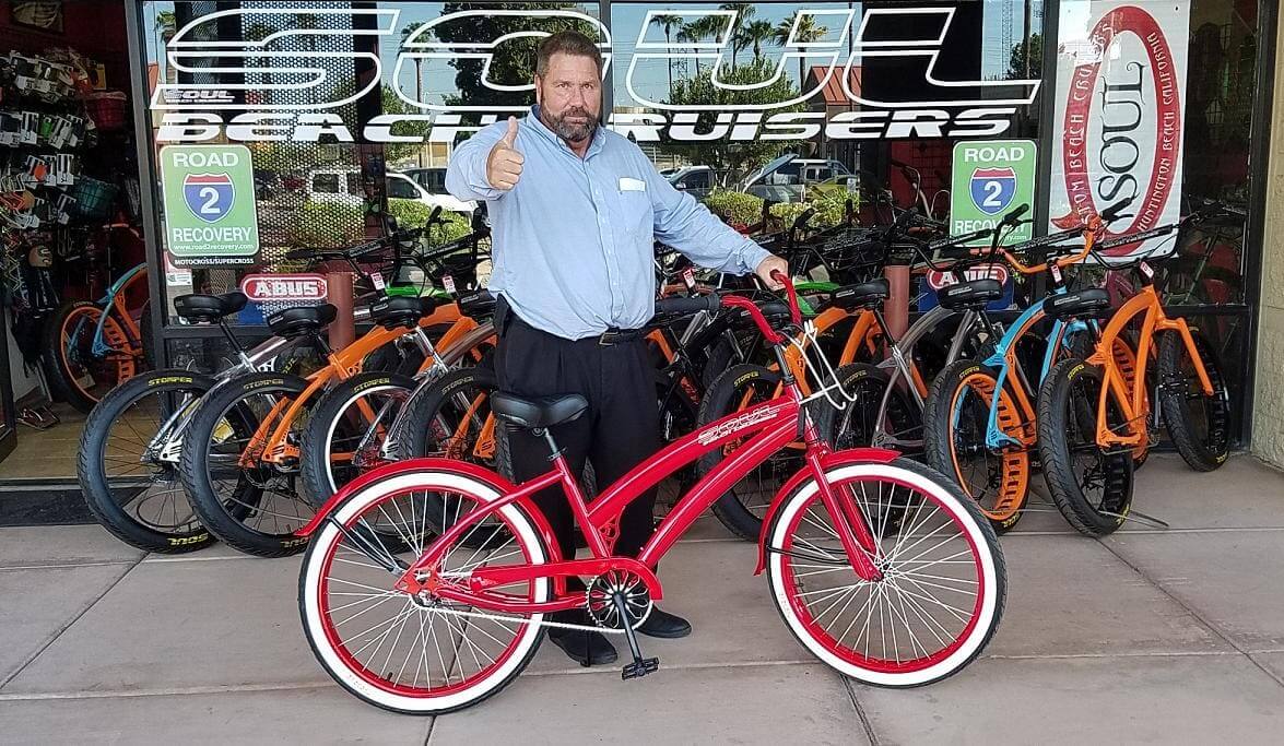 Man posing with red beach cruiser bicycle.