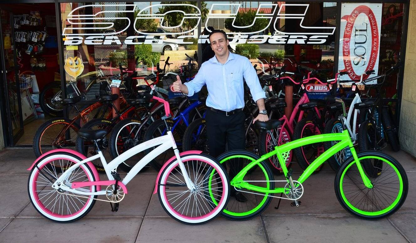 Man smiling with colorful bicycles outside shop.