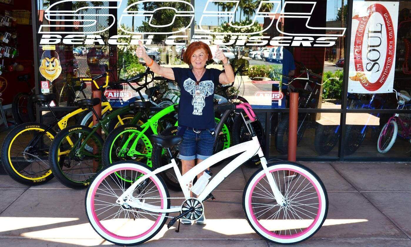Woman posing with white bicycle outside shop.