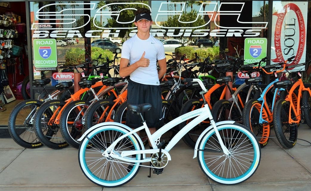 Person with white bicycle outside bike shop.