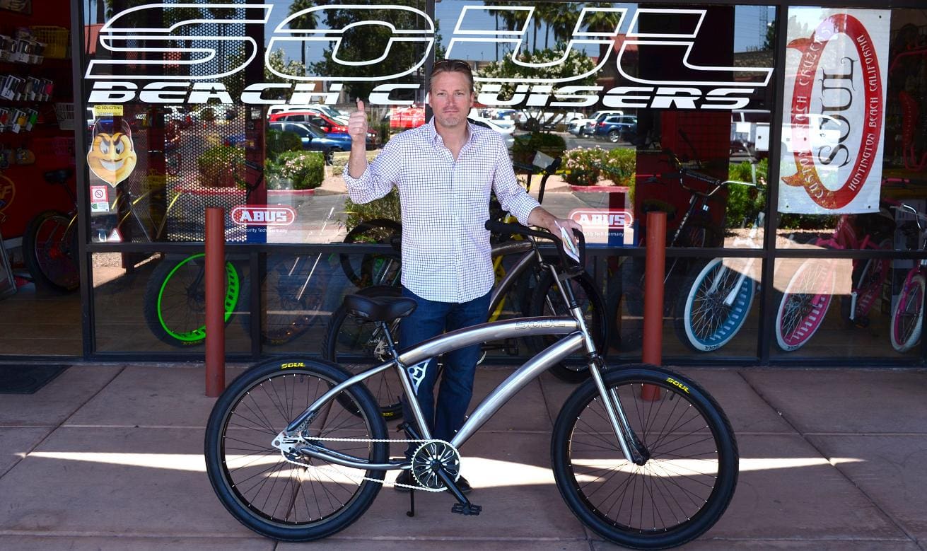 Man standing with bicycle outside bike shop.