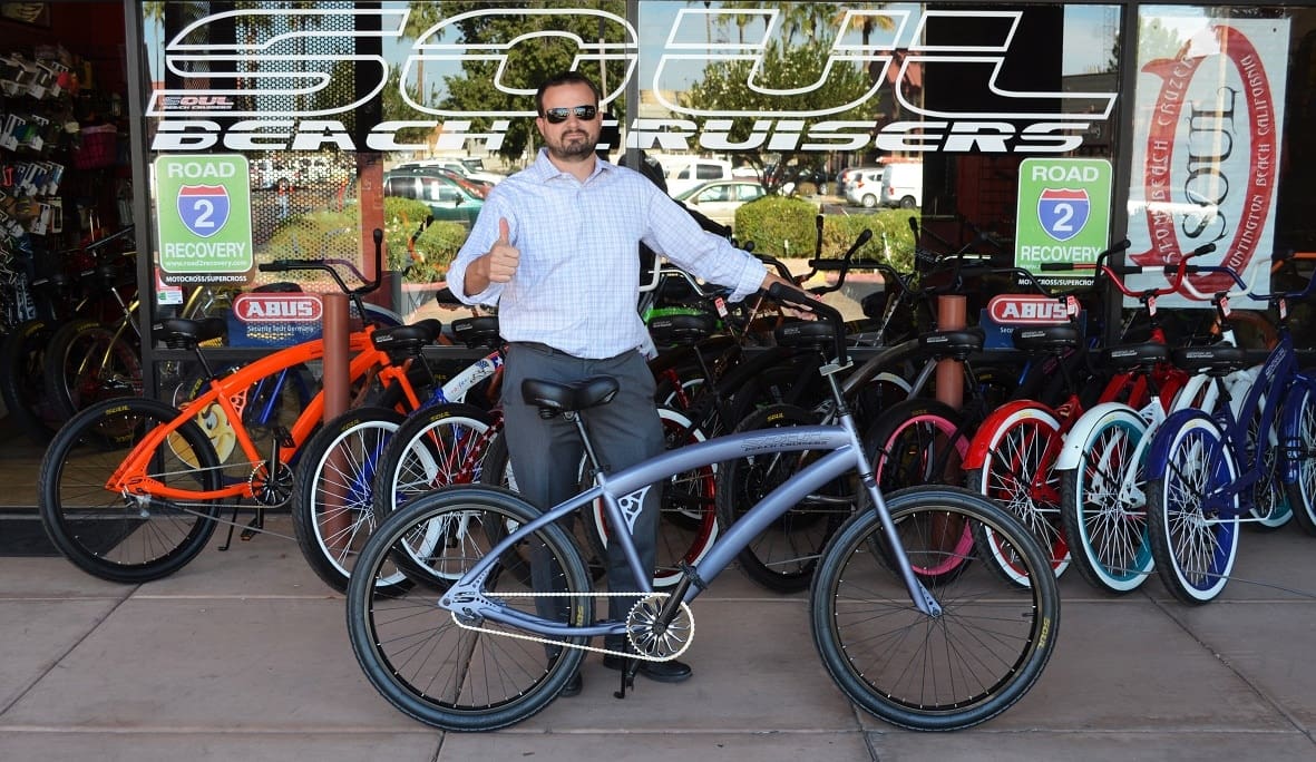 Man giving thumbs up with bicycle outside shop.