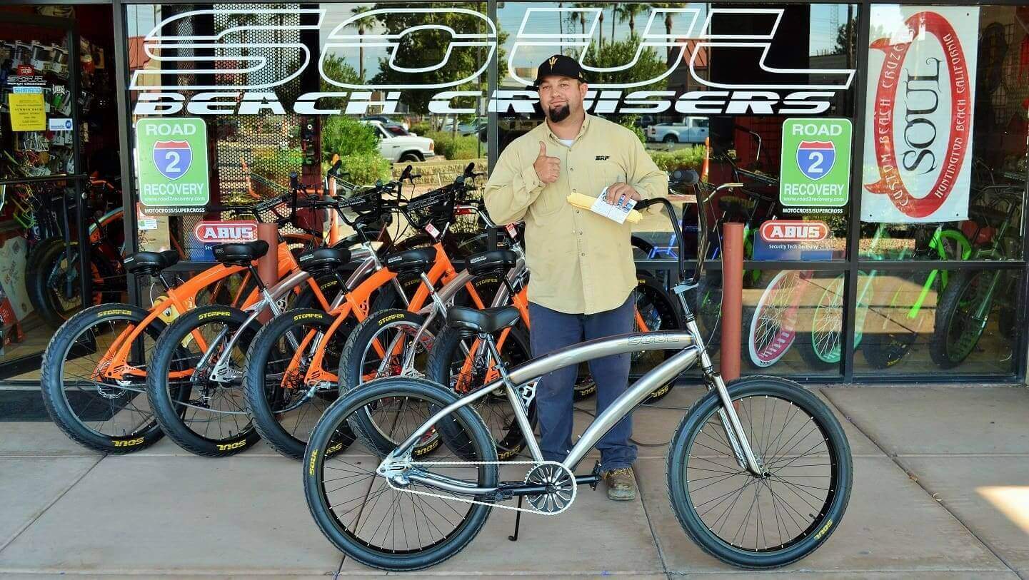 Man standing with bicycles outside bike shop.