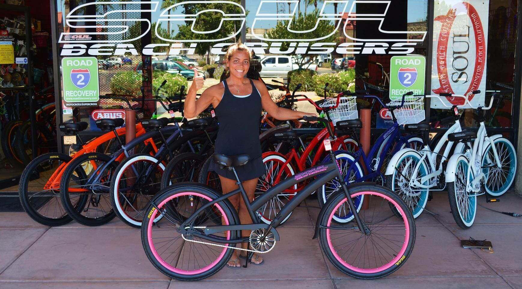 Woman posing with bicycle at store entrance.