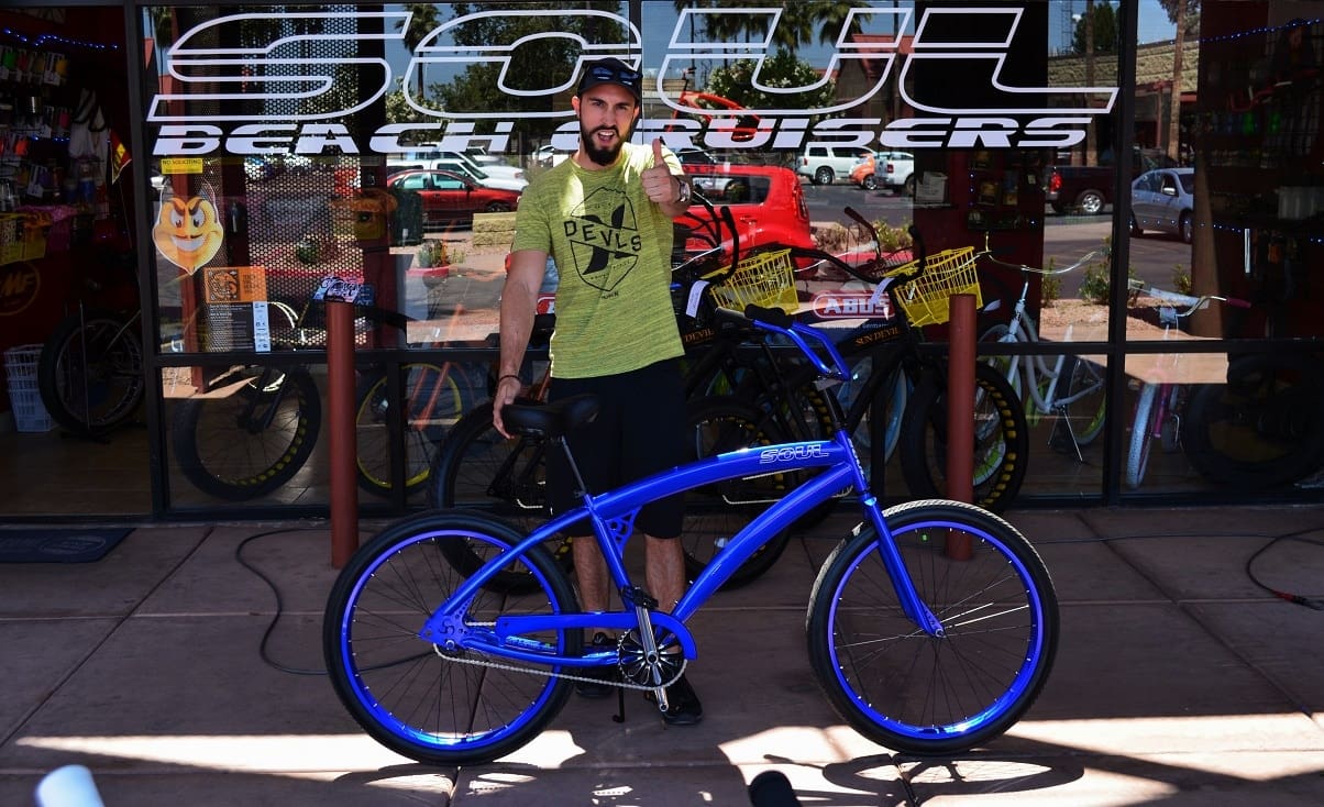Man with blue bicycle outside bike shop.