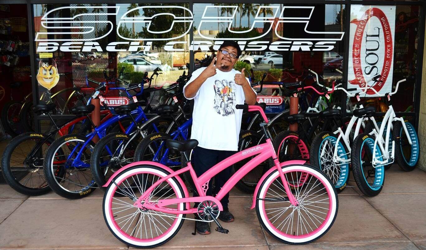 Man posing with pink bicycle at shop.