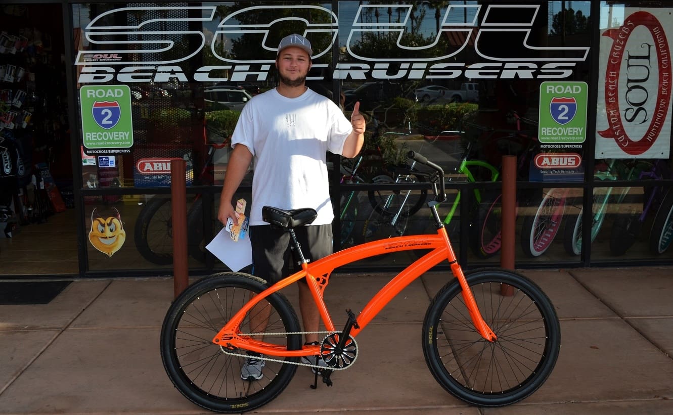 Man with orange bicycle in front of store.