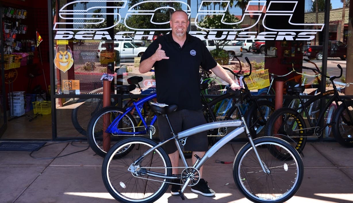 Man posing with bicycle outside shop.