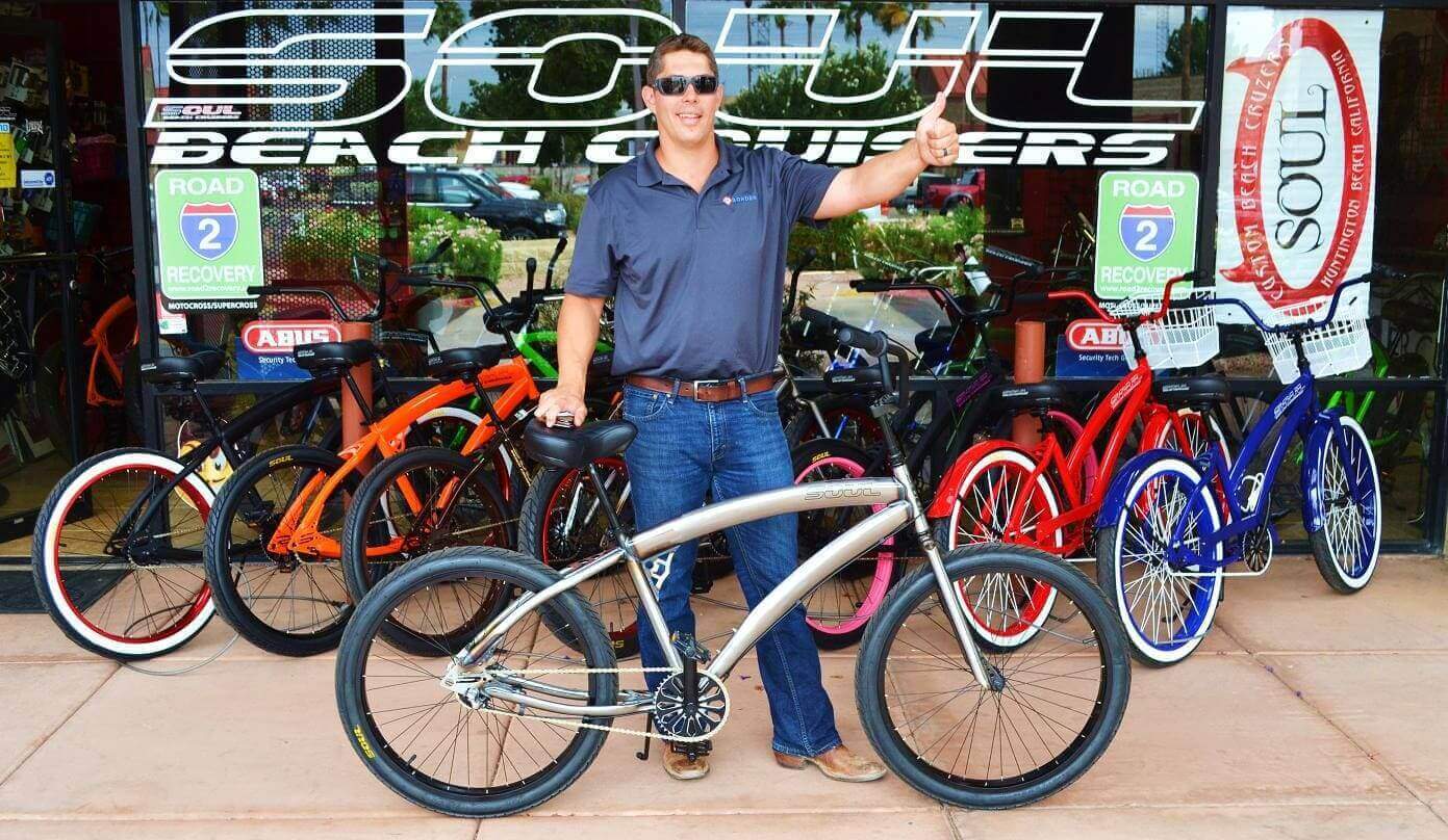 Man posing with bicycle in front of shop.