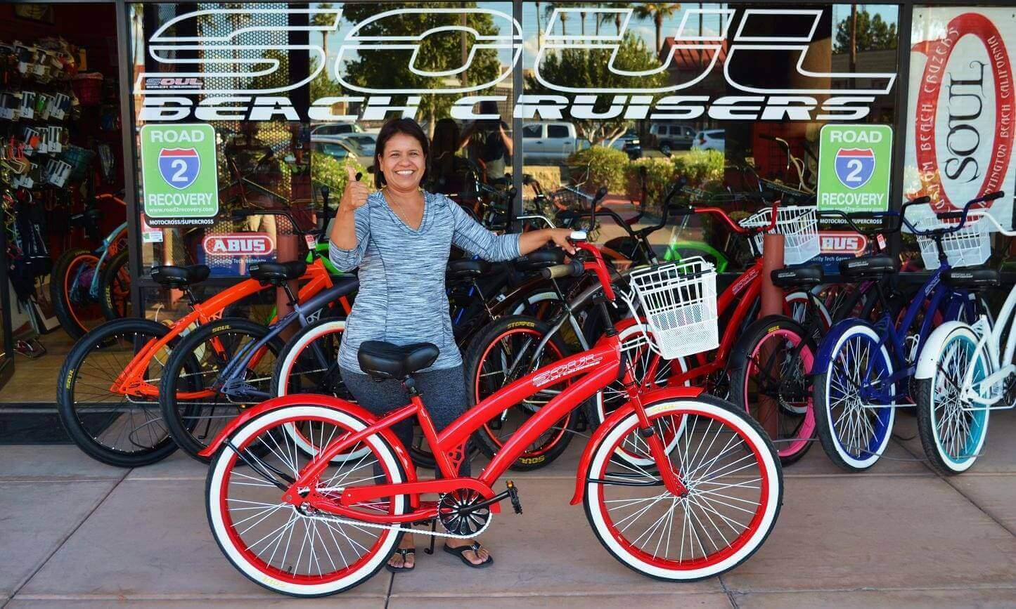 Woman with red bike outside bicycle shop.