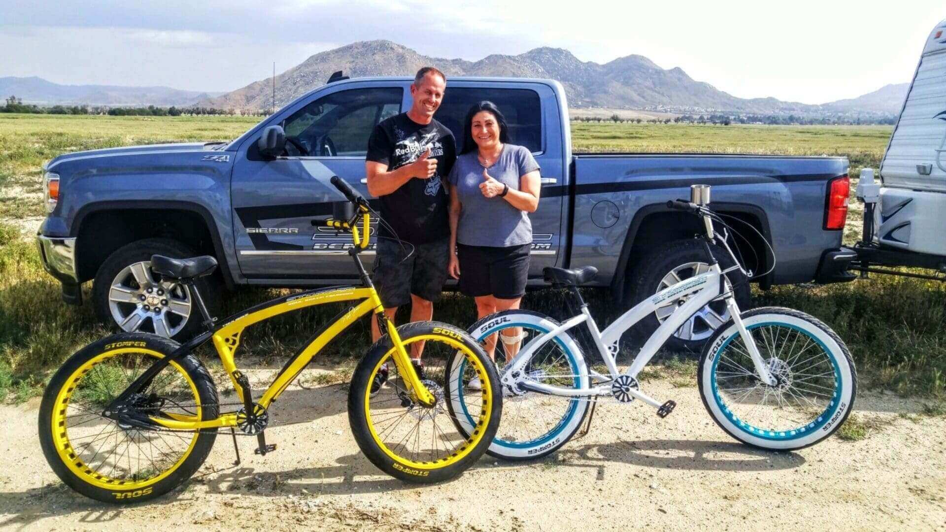 Couple posing with bicycles and truck outdoors.