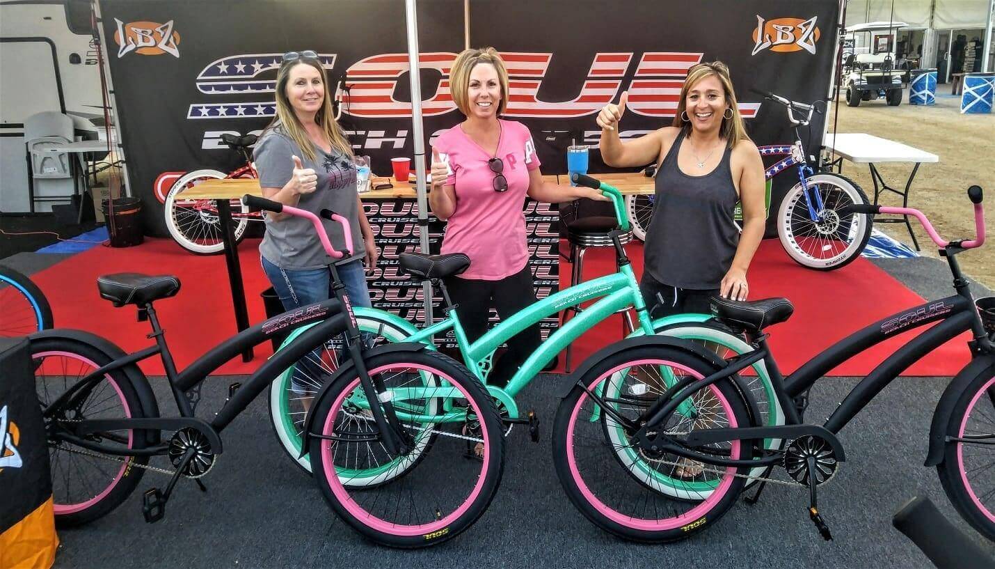 Three women posing with colorful bicycles.
