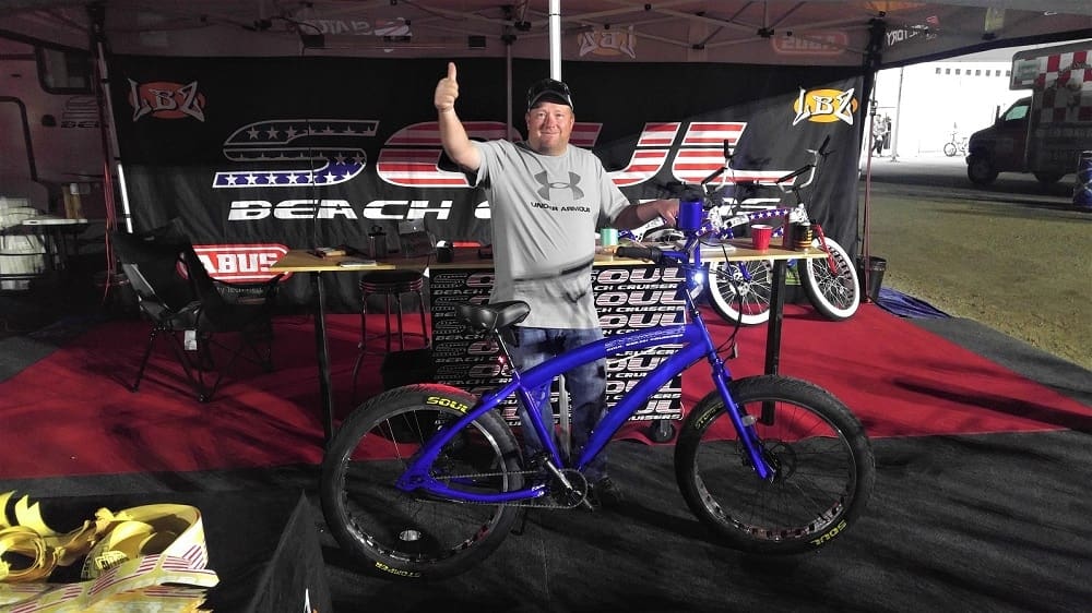 Man posing with blue bicycle at event.