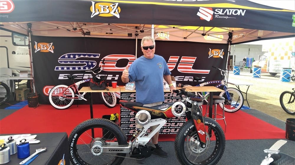 Man posing with electric bicycle at booth.