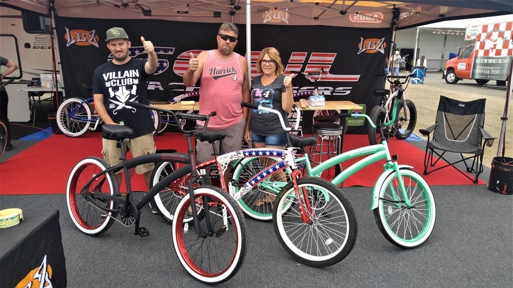 Three people displaying colorful custom bicycles.