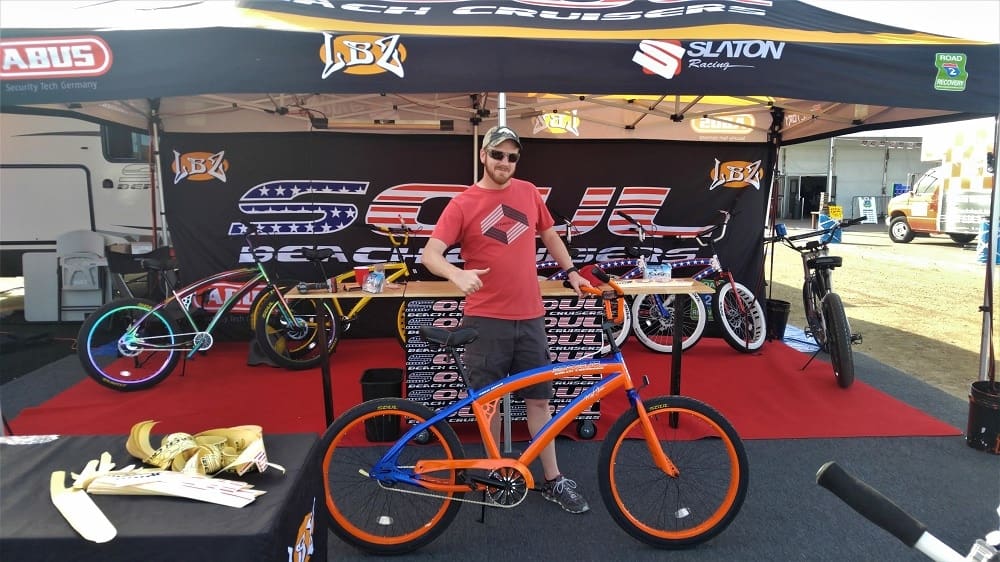 Man posing with bikes at outdoor booth.