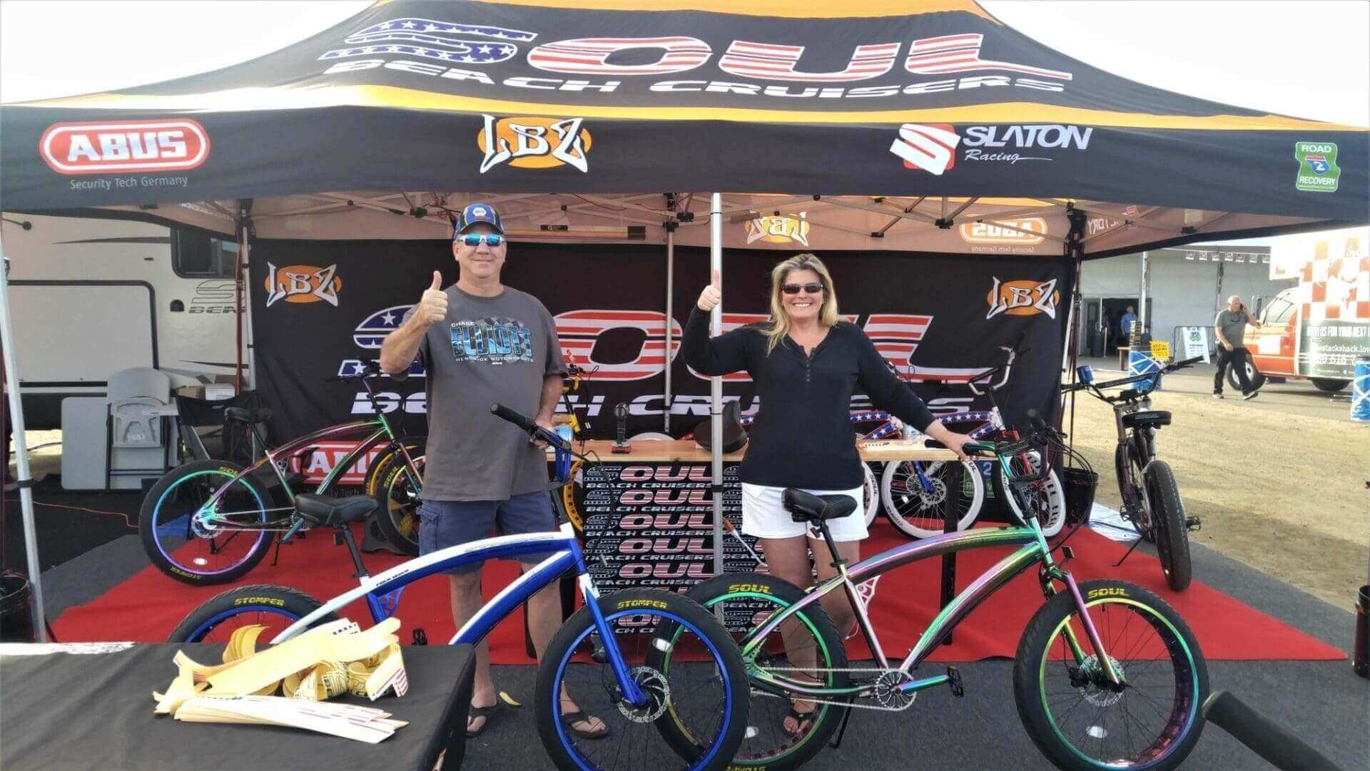 People posing with bicycles under event tent.