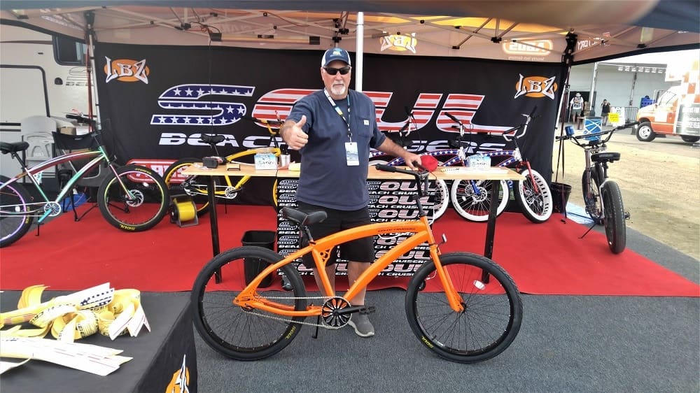 Man posing with orange bike at booth.
