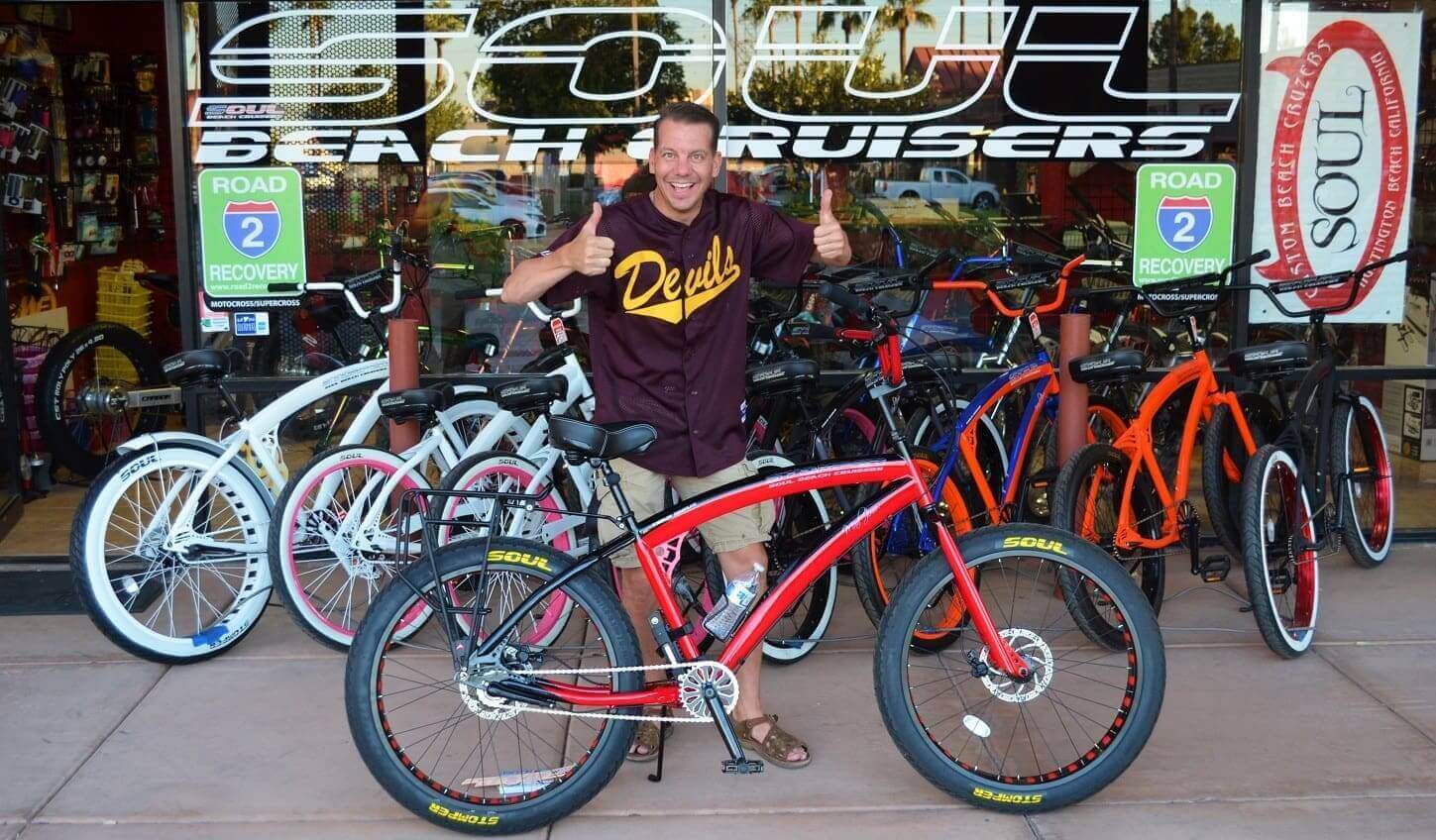 Man posing with bicycles outside shop.