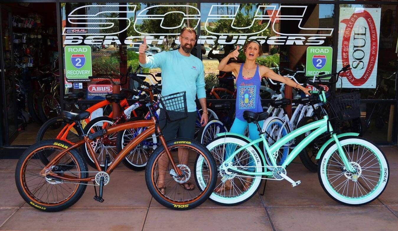 People posing with beach cruiser bicycles outside store.