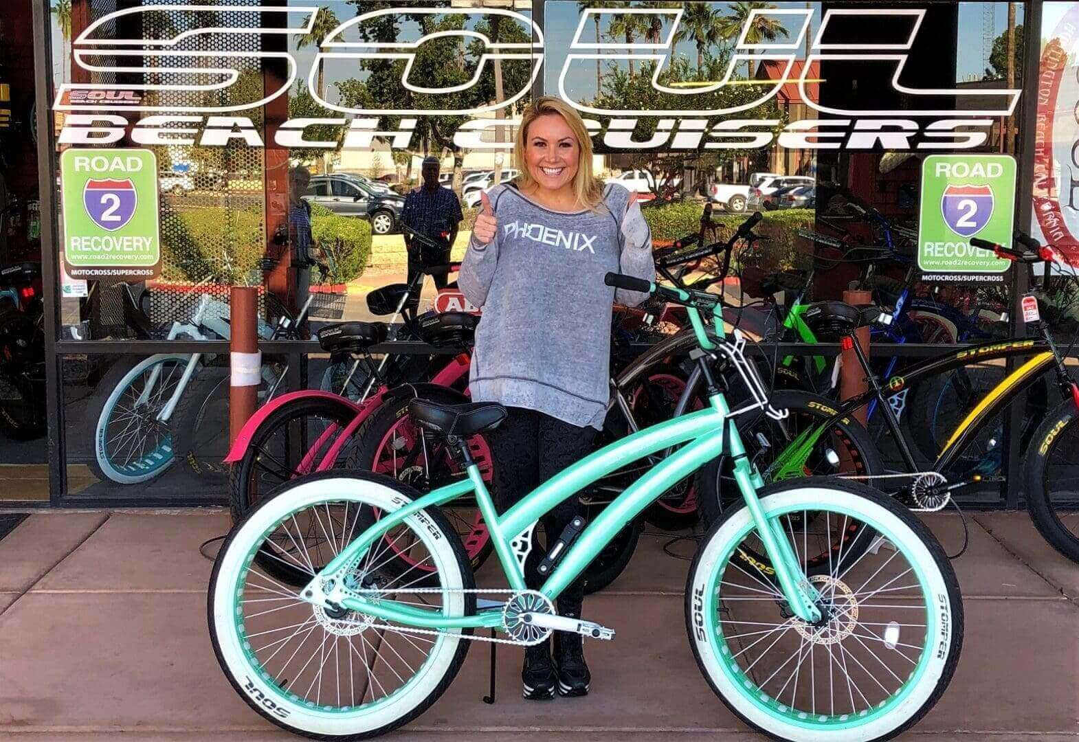 Woman smiling with teal bicycle outside shop.