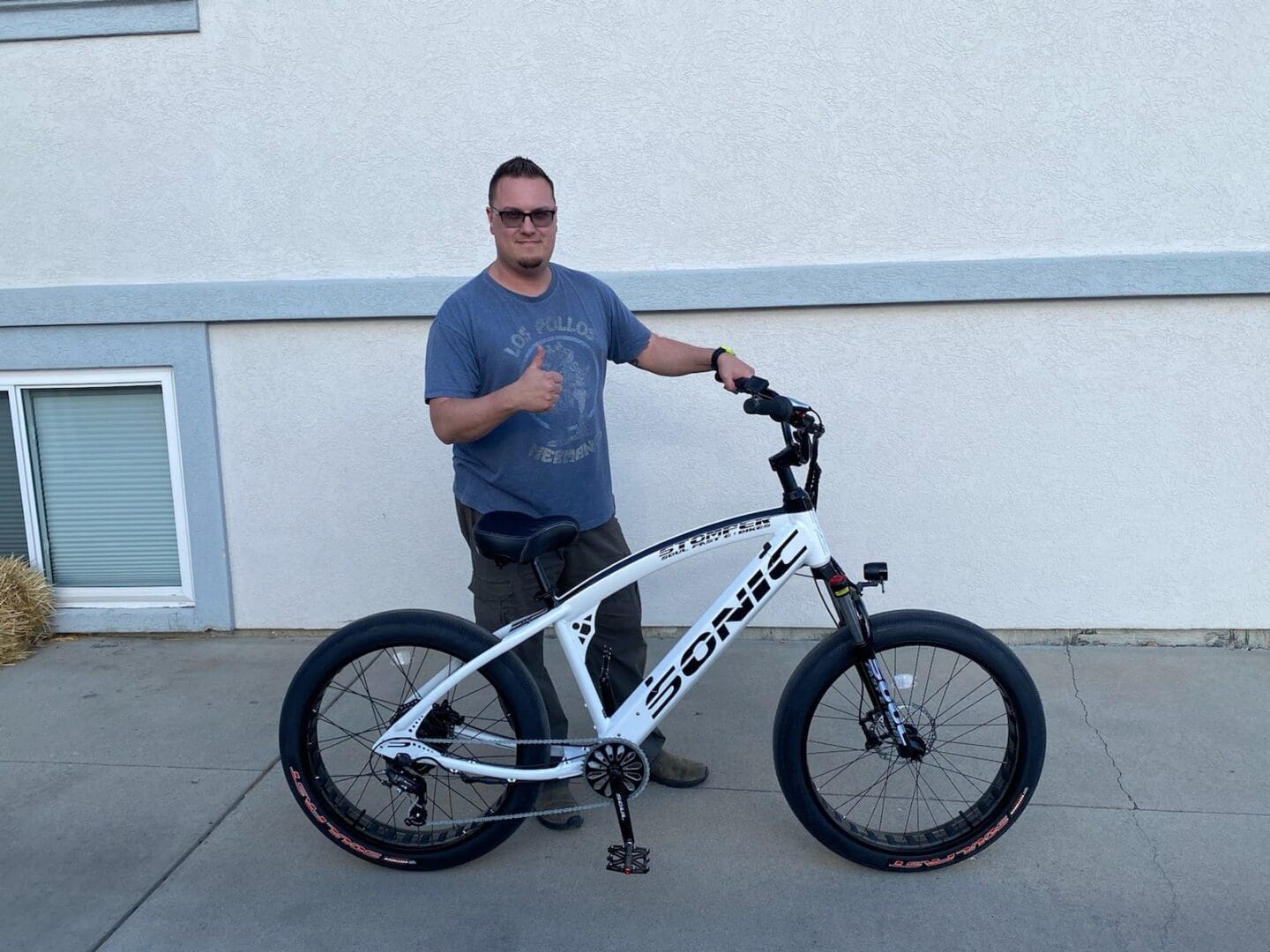 Man posing with white electric bicycle outside.