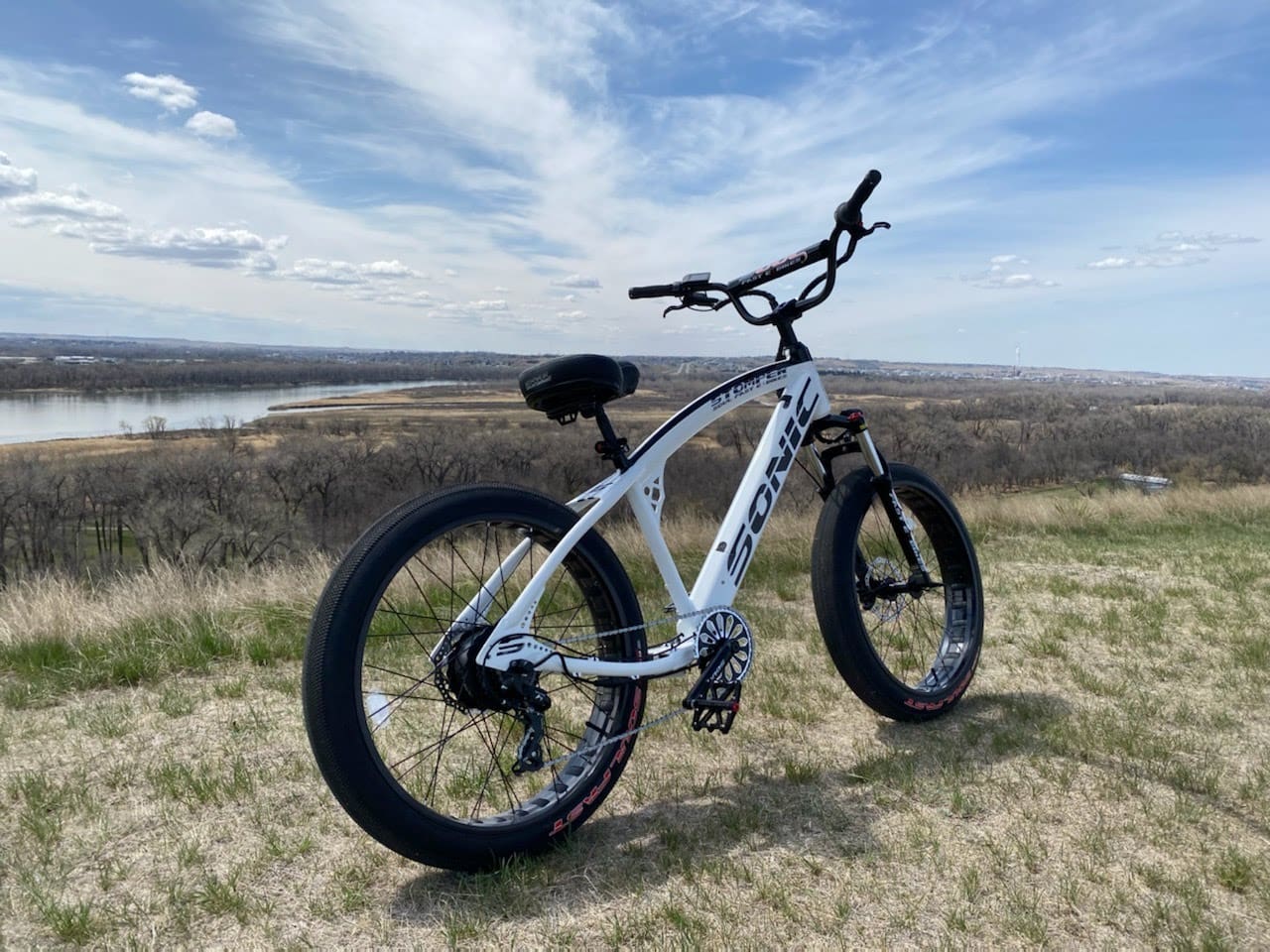 White bicycle on grassy hill with sky.