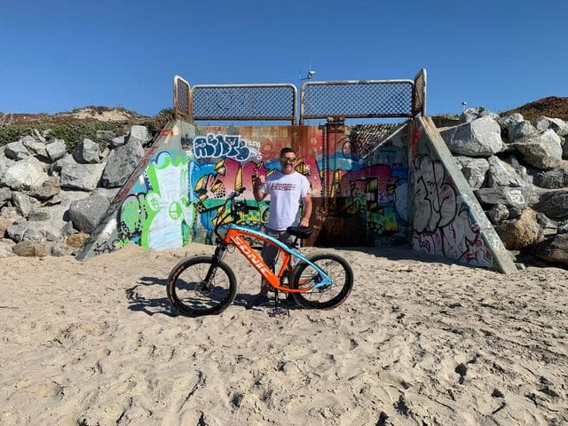 Man with bike in front of graffiti wall.