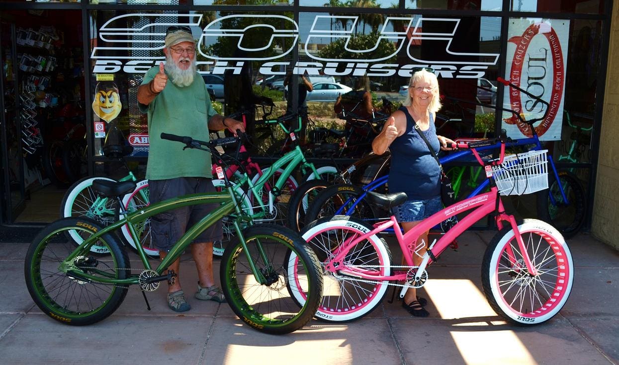 People with colorful bikes outside bicycle shop.