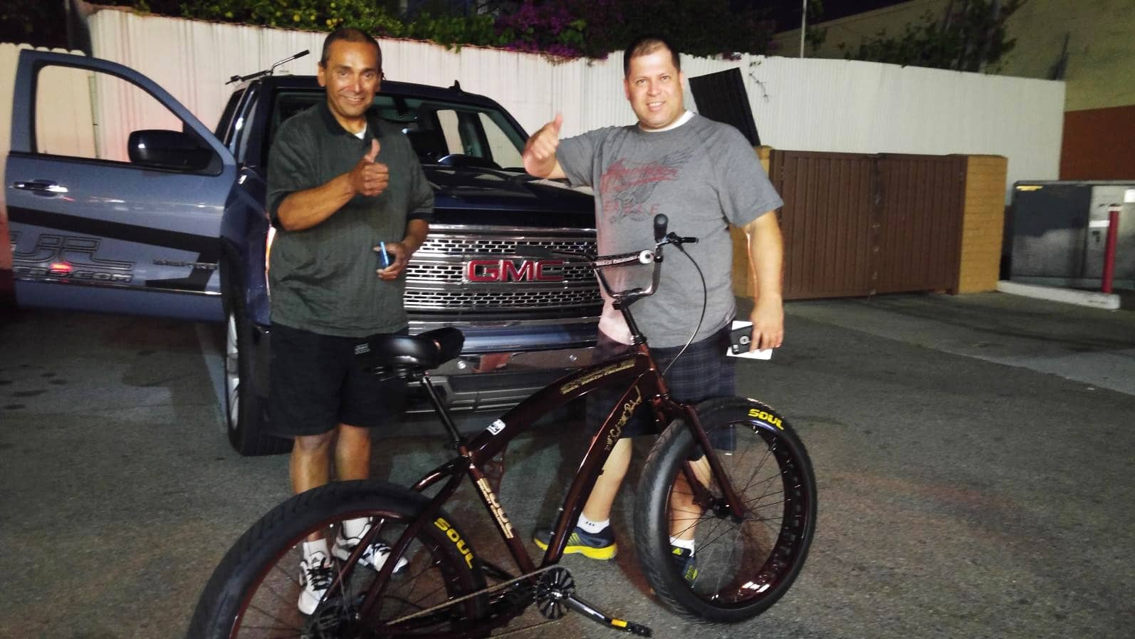 Two men with bicycle in front of truck.
