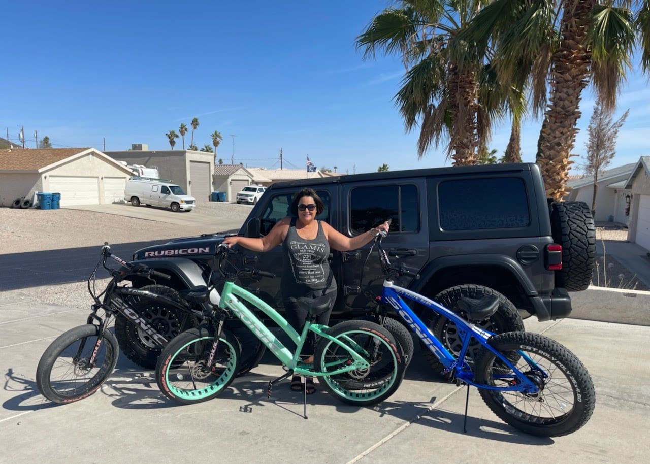 Woman posing with bikes and Jeep outdoors.