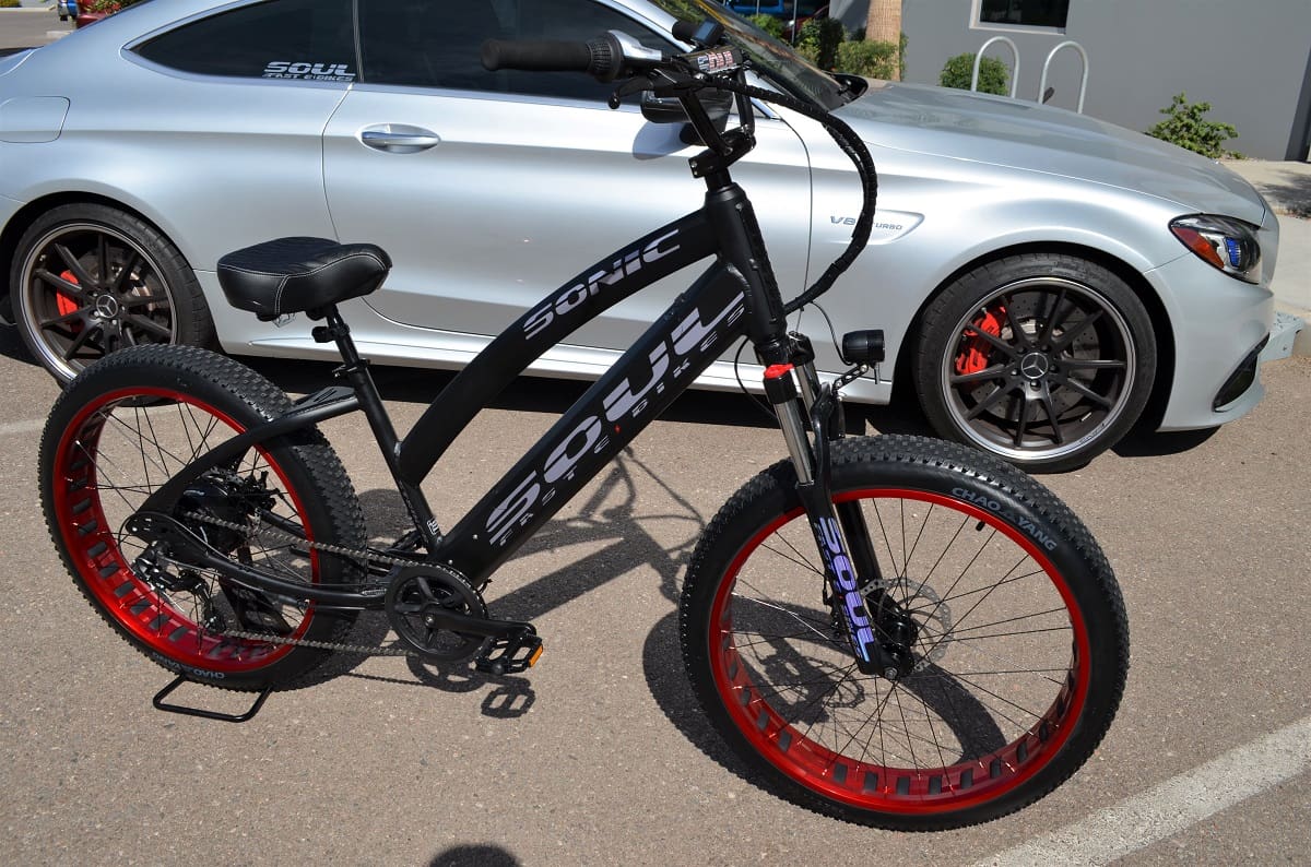 Electric bicycle beside a silver sports car.