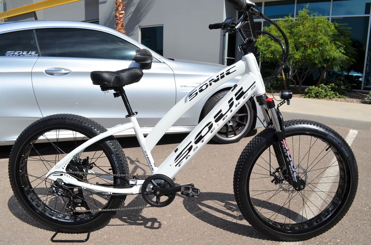 White electric bicycle parked beside car.