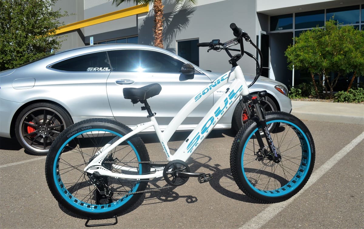 White bicycle parked beside a silver car.
