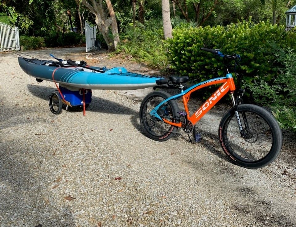 Bicycle towing kayak on gravel path.