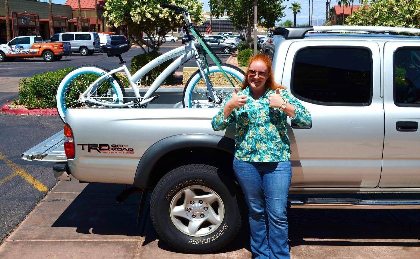 Woman smiling beside truck with bicycle.