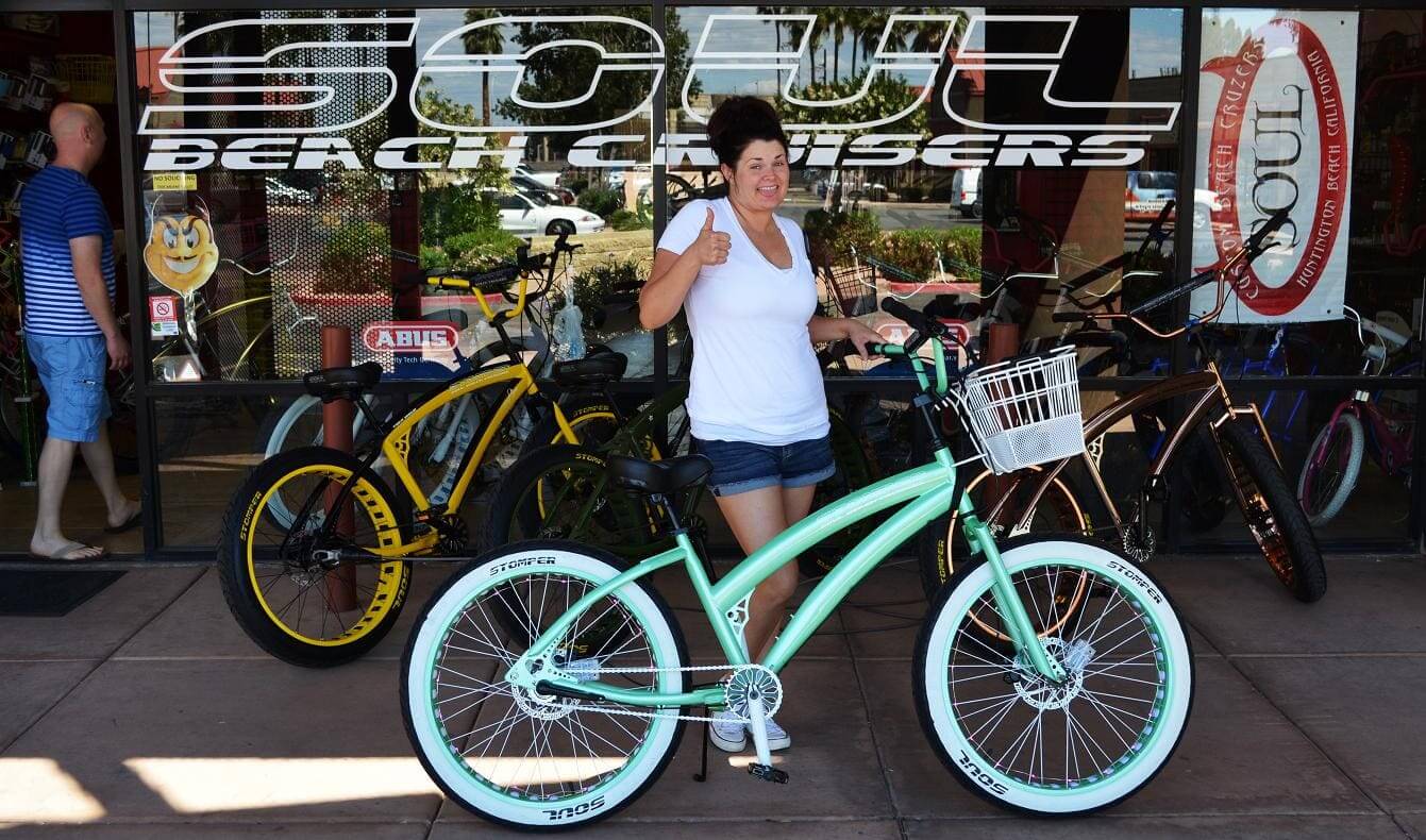 Woman with mint green bicycle outside store.