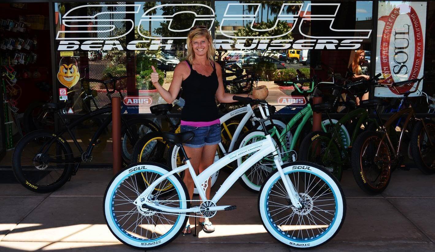 Woman smiling with white beach cruiser bicycle.