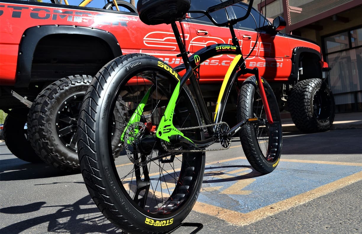 Bicycle with large tires near lifted truck.