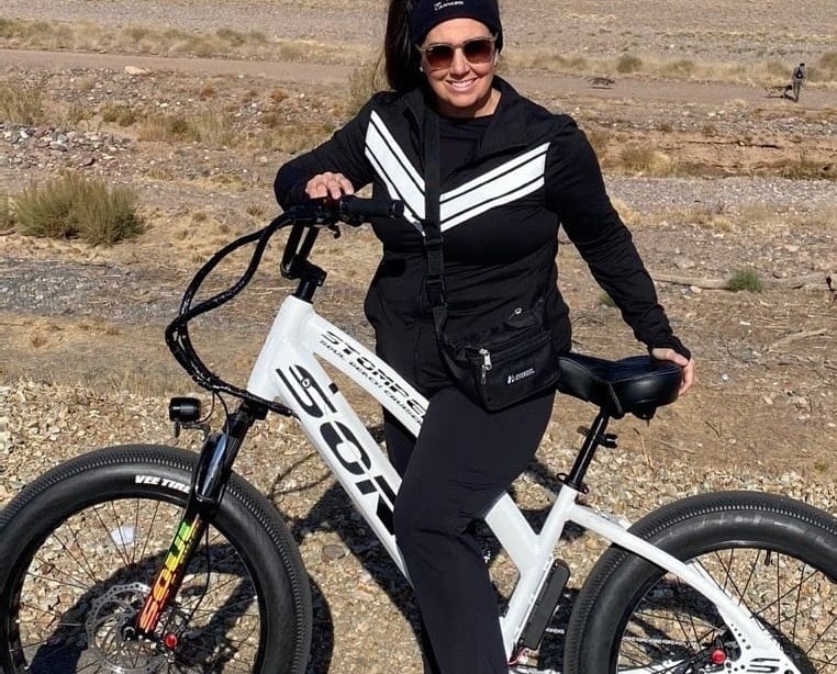 Woman posing with a bicycle outdoors.