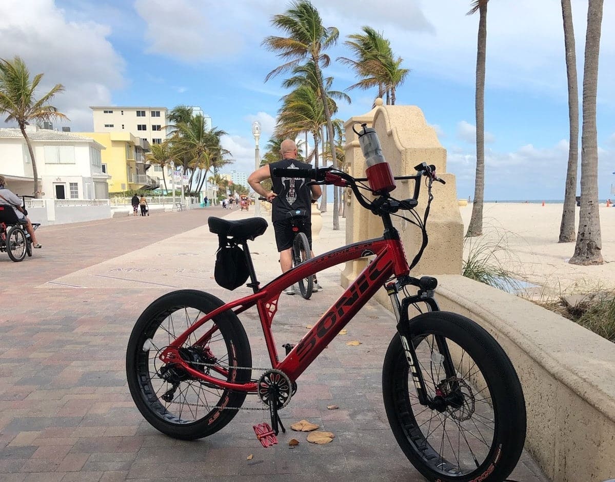 Red bike parked on beachfront promenade.