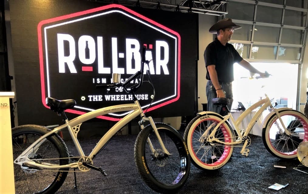 Man with bicycles in front of Roll-Bar sign.