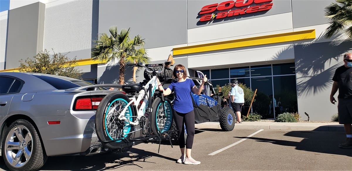 Woman with bikes on car rack outdoors.