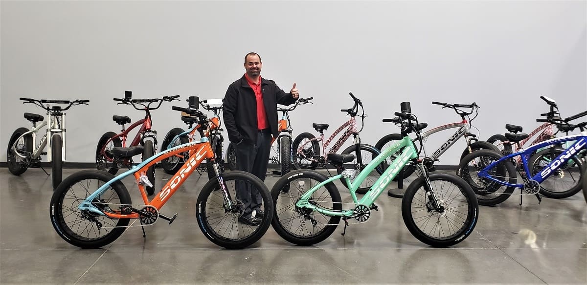 Man posing with colorful electric bicycles indoors.