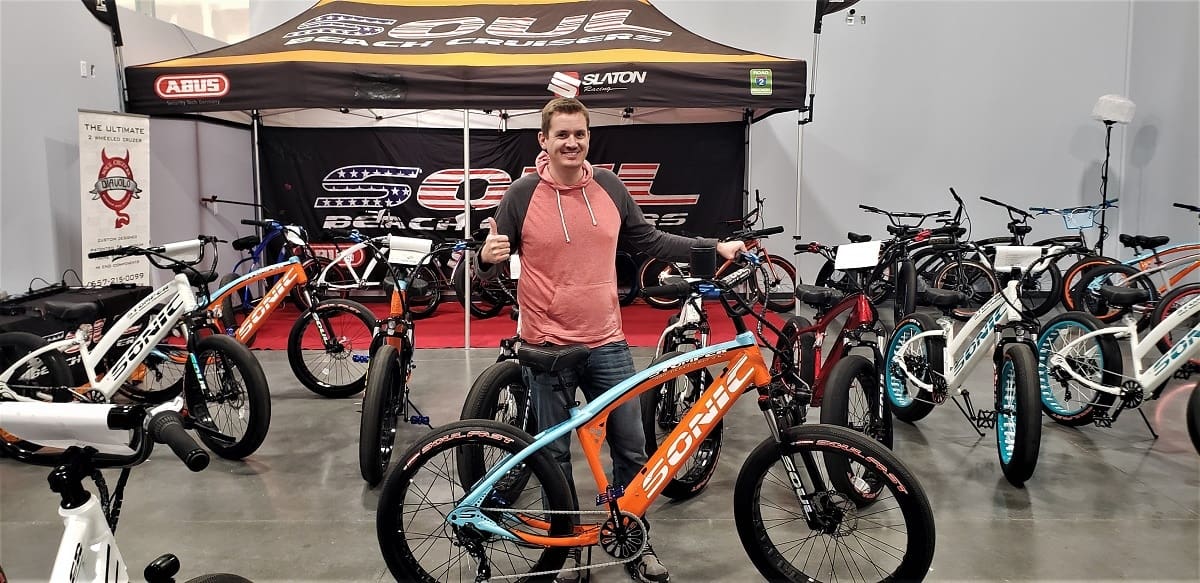 Man posing with bicycles at a bike expo.