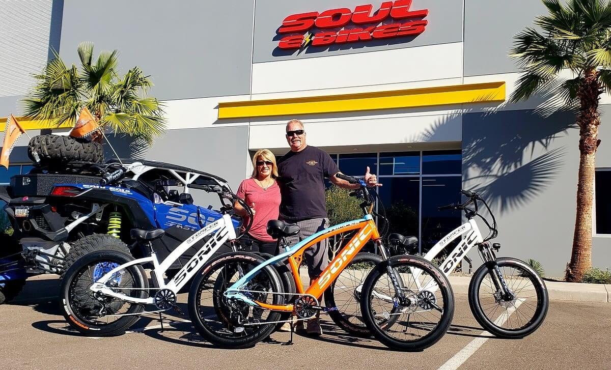 Couple standing with bikes outside store.