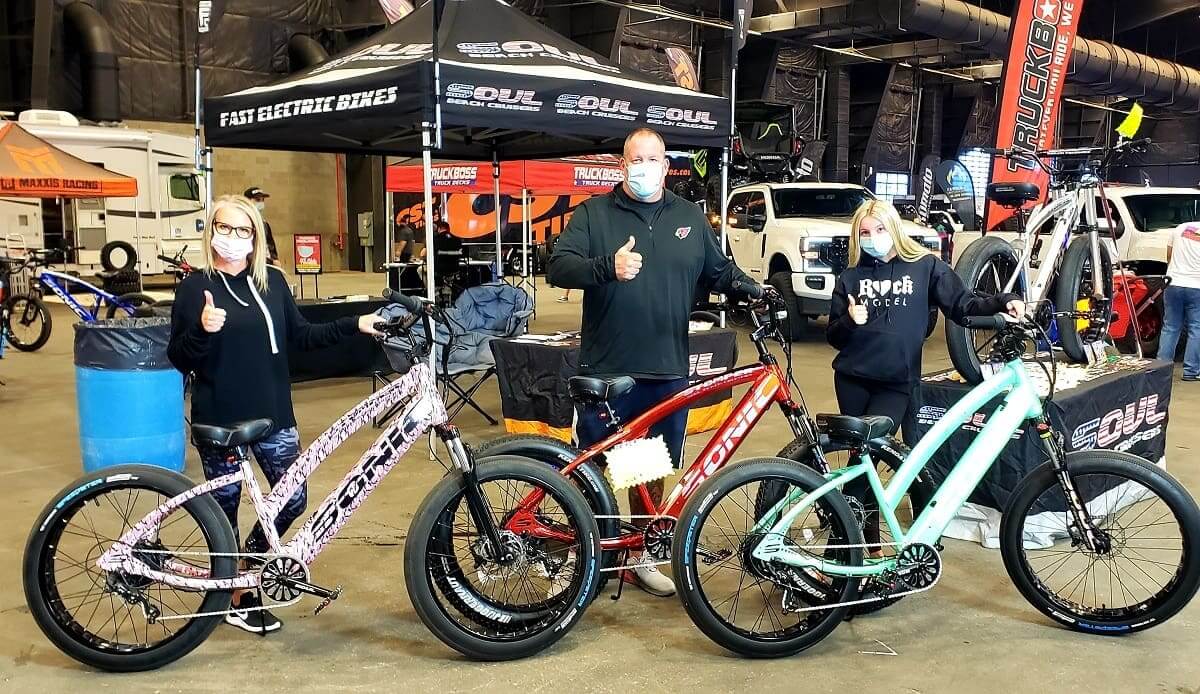 People with electric bikes at indoor event.